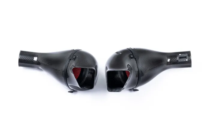 Two black, carbon-fiber air intakes with red filters are placed side by side on a white background, displaying their sleek, aerodynamic design.