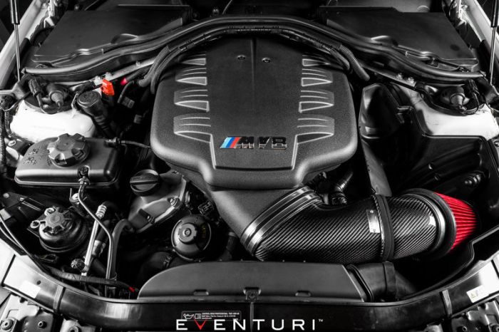 Engine bay featuring a BMW V8 engine with "M Power" branding on the cover. The Eventuri carbon fiber intake system with a red air filter is prominently visible.