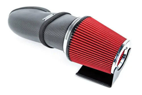 A red and black cone-shaped air filter attached to a carbon fiber intake system, resting on a white surface.