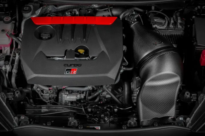 A black engine with a red accent labeled "turbo" and "GR" is mounted in a car's engine bay, surrounded by various mechanical components and wiring.