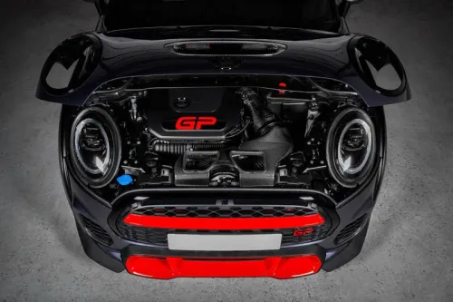 A car with an open hood displays a compact engine labeled "GP" in red, featuring prominent headlights and red accents, situated in a well-lit garage setting.