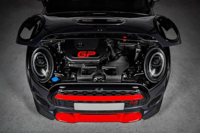 A car with an open hood displays a compact engine labeled "GP" in red, featuring prominent headlights and red accents, situated in a well-lit garage setting.