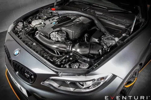 A BMW car engine featuring a carbon fiber intake system is displayed in a showroom. The hood is open, exposing the engine components. The brand name "EVENTURI" is visible at the bottom.