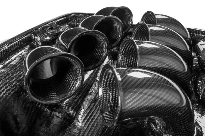 Glossy black carbon fiber intake trumpets are arranged close together, nestled within a molded carbon fiber base, reflecting studio lights.
