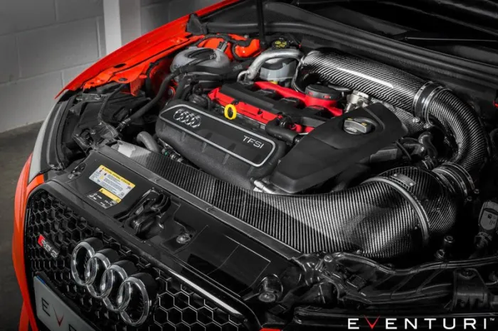 Car engine with a prominently branded logo and red-highlighted parts, surrounded by glossy carbon fiber components in a well-lit garage. Text: "EVENTURI" and "TFSi."