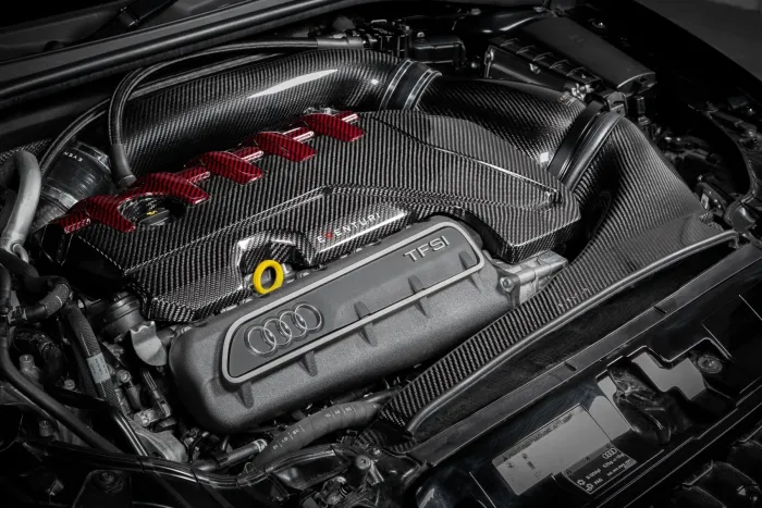 A car's Audi TFSI engine, covered in carbon fiber components and red accents, sits within a clean, organized engine bay.