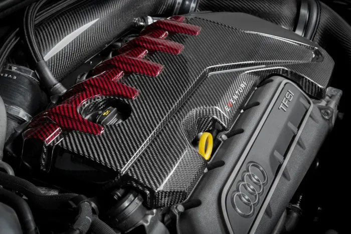 A carbon fiber engine cover with red accents, labeled "EVEN-TURI" over a TFSI engine in an Audi car, surrounded by black hoses and components.