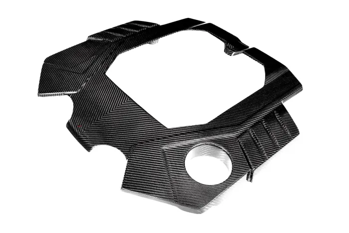 A carbon fiber engine cover with precisely cut edges and a textured pattern is shown against a white background, designed to fit specific mechanical components.