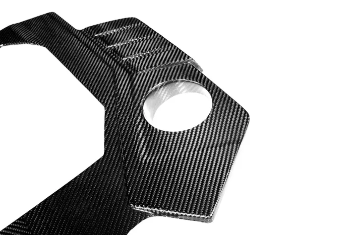 A carbon fiber component with a sleek surface features a circular cutout and angled edges, against a plain white background.