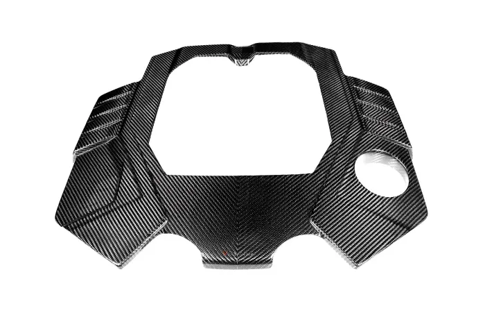 Carbon fiber engine cover with a central cutout and rounded edges, featuring angular patterns; placed against a plain white background.