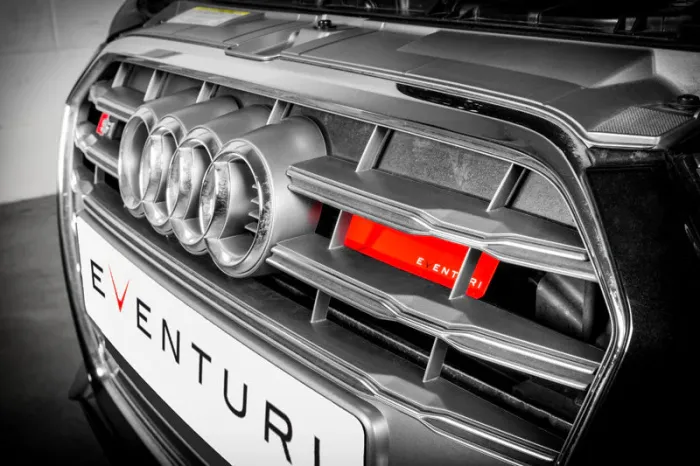 Car grille with four circular vents featuring the Audi logo and a red 'EVENTURI' branded filter, set within a modern garage environment. The license plate reads "EVENTURI".