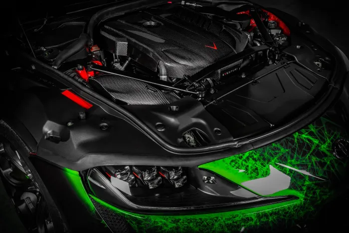A high-performance car's engine bay, featuring a carbon fiber engine cover with "Eventuri" branding, surrounded by black and red components, and a green, geometric-patterned front body.