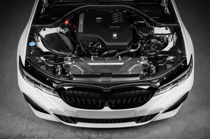BMW car engine with visible branding, situated under an opened hood, in a clean, white car body, viewed from the front in an indoor setting. Text: "BMW" and "TwinPower Turbo."