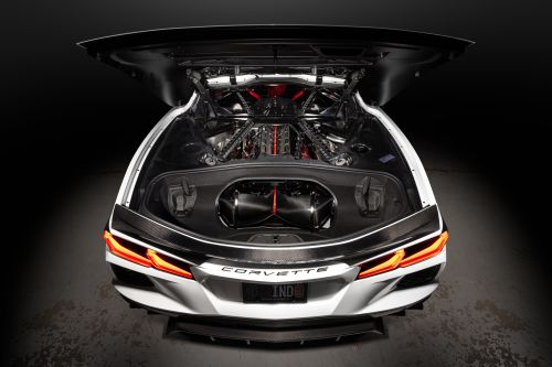 A white Corvette showcases its powerful engine under an open hood in a dimly lit garage. Text reads "CORVETTE" on the rear.