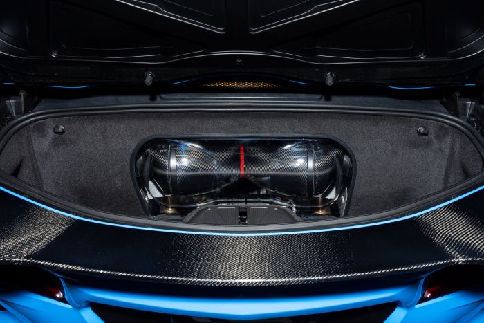 Carbon fiber air intake, enclosed in a clear casing, sits inside the trunk of a high-performance car with visible blue bodywork and black interior lining.