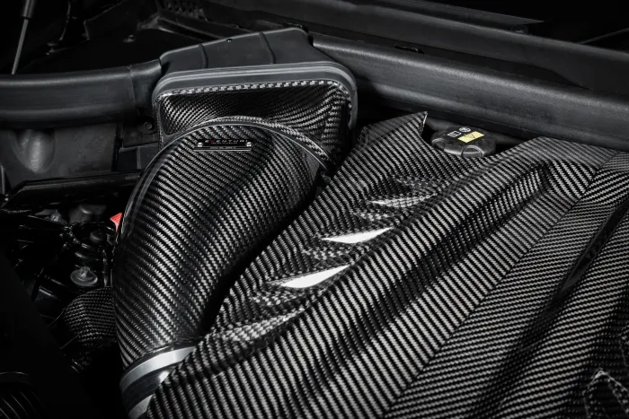 Carbon fiber engine components showcased in an intricately designed vehicle engine bay, illuminated under strong lighting, revealing the texture and detail of the carbon fiber material.