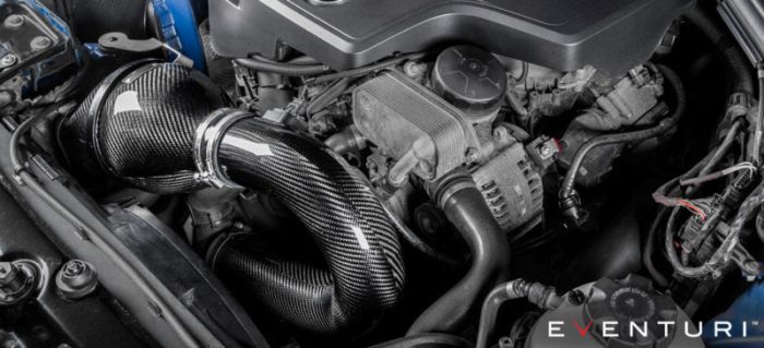 A carbon fiber air intake system is installed in a car engine bay surrounded by various engine components. The image text reads "EVENTURI™".