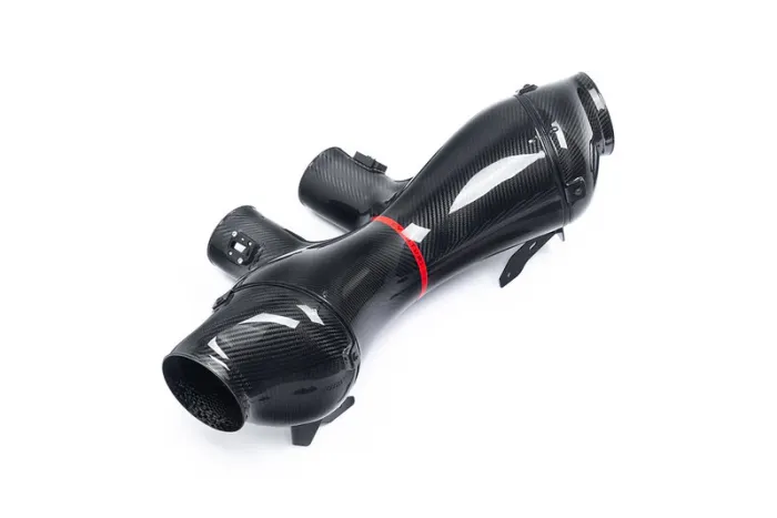 A black carbon fiber automotive air intake system lies on a white background. It features multiple connecting points and a red band near its center.