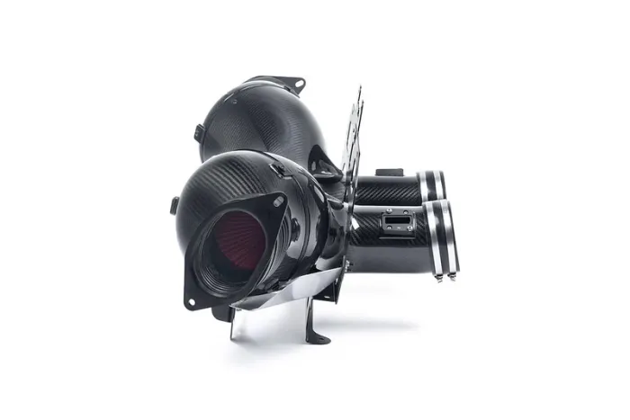 A black, carbon-fiber automotive air intake system with dual cylindrical components and metallic clamps is depicted on a white background.