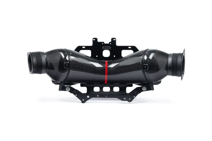 A carbon fiber automotive intake assembly with a central red stripe rests on a black mounting bracket, positioned against a plain white background.