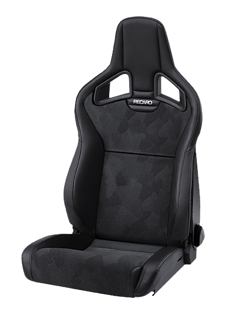 A black Recaro racing seat with adjustable components rests against a plain background. The seat features a high back, integrated headrest, and patterned fabric upholstery with ergonomic contours.