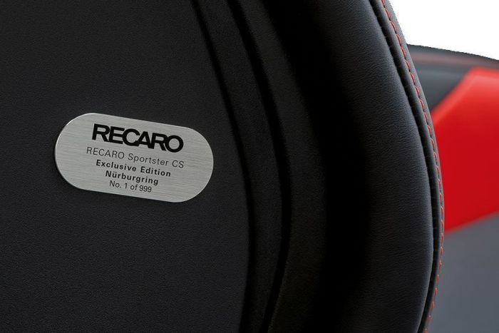 A close-up of a black car seat features a metallic plaque that reads: "RECARO Sportster CS Exclusive Edition Nürburgring No. 1 of 999." Red stitching and background are partially visible.