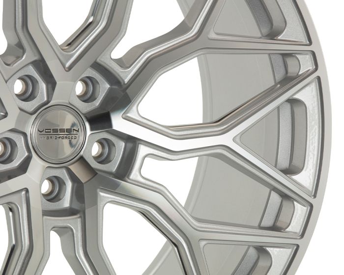 A metallic car wheel rim, intricately designed with multiple spokes, features the engraved text "VOSSEN HYBRID FORGED" at its center, against a neutral background.