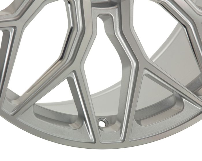 A metallic wheel rim features an intricate, angular spoke design in a smooth, silver finish, set against a plain white background.