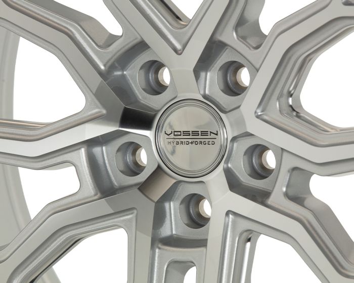 A silver alloy wheel features a polished, multi-spoke design. The center cap displays "VOSSEN HYBRID FORGED" text, highlighting its brand and manufacturing technique.