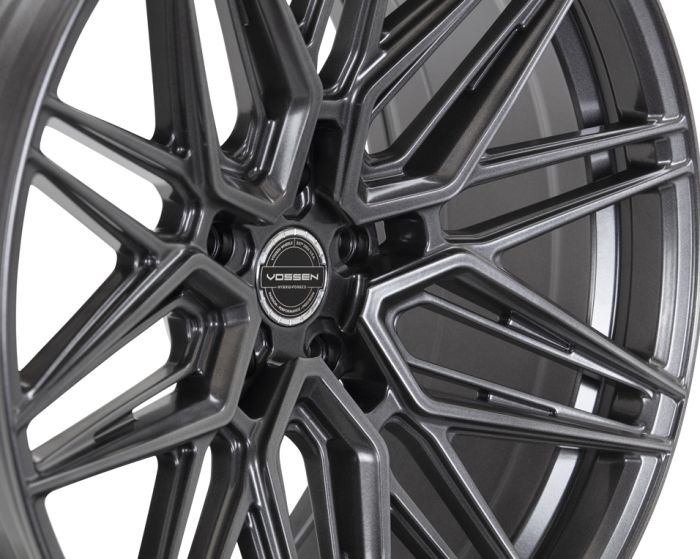 A matte black alloy wheel with intricate, web-like spokes prominently displays a central cap reading "VOSSEN," set against a plain, light background.