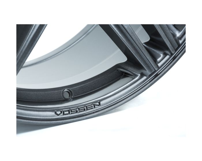 A metallic wheel rim with stylized grooves features the embossed text “VOSSEN” along its edge, set against a white background.