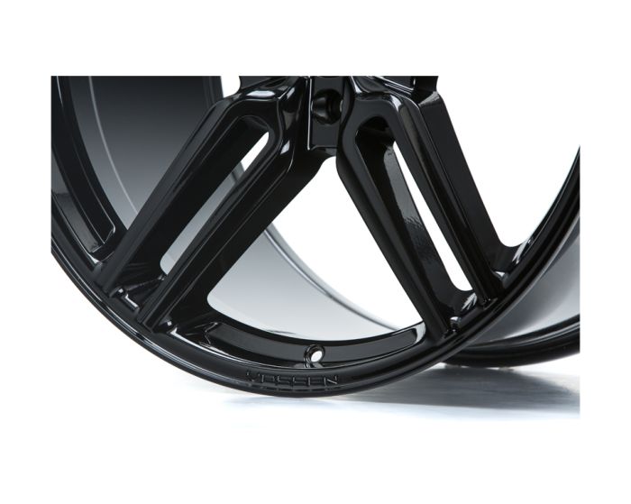 A glossy black car wheel rim with a modern, angular design rests against a plain white background. The word "VOSSEN" is etched into the rim's edge.