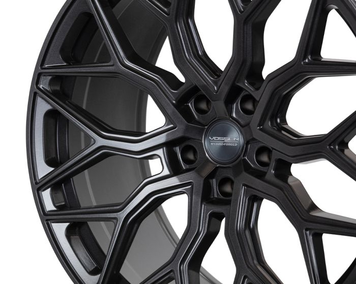 A black alloy wheel with an intricate, multi-spoke design is displayed prominently. The center cap reads "VOSSEN HYBRID FORGED." The background is plain, emphasizing the wheel's details.