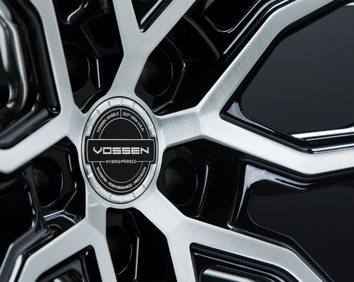 A metallic car wheel with a sleek, multi-spoke design features a central emblem reading, "VOSSEN HYBRID FORGED," surrounded by text: "VOSSEN WHEELS," "ESTP 2006 USA," "PASSION - PERFORMANCE - PRECISION."