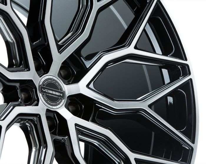 A black and silver alloy wheel is displayed featuring intricate spoke design, with the center cap reading "VOSSEN HYBRID FORGED" against a plain white background.