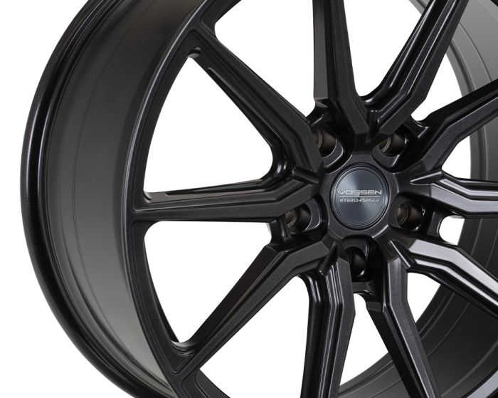 A sleek black automotive wheel features a multi-spoke design with a polished finish. The hubcap displays the text "VOSSEN HYBRID FORGED," emphasizing its brand and manufacturing process.