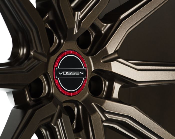 Bronze alloy wheel with angular spokes radiating from a center hub labeled "VOSSEN," set against a plain, dark background.