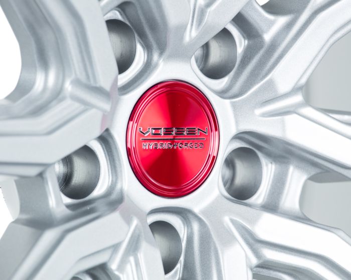 Silver alloy wheel rim featuring a red center cap with the text "VOSSEN HYBRID FORGED" embossed, highlighting intricate spokes and metallic texture.