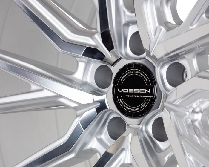 A polished silver alloy wheel showcases its intricate design in a well-lit studio. Center cap displays: "VOSSEN HYBRID FORGED, VOSSEN WHEELS, ESTD. 2006 USA, PASSION - PERFORMANCE - PRECISION."