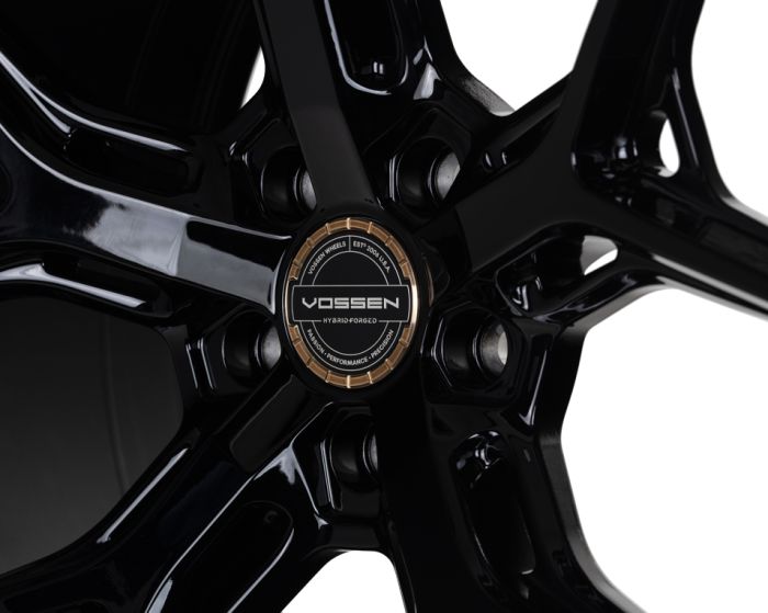 A glossy black alloy wheel features a central logo with text: "VOSSEN HYBRID FORGED, VOSSEN WHEELS EST 2006 U.S.A, FREEDOM · PERFORMANCE · PRECISION," set against a shiny metal background.