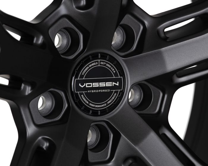 A black alloy wheel showcases a central circular hub with the text: "VOSSEN WHEELS ESTP 2006 U.S.A. VOSSEN HYBRID-FORGED PASSION · PERFORMANCE · PRECISION," set against a sleek, metallic background.