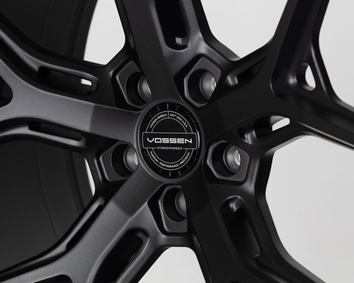 A black alloy wheel with a five-spoke design, centered on a hubcap labeled "Vossen Hybrid Forged," surrounded by text: "Vossen Wheels Est. 2006 U.S.A. Passion • Performance • Precision."