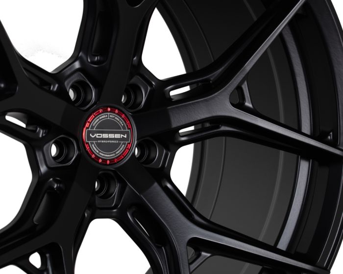 Black alloy wheel with five spokes, labeled "VOSSEN HYBRID FORGED" in the center, surrounded by a red ring. Set against a white background.