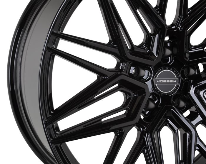 A glossy black alloy wheel rim with intricate, geometric spokes. The center displays the logo "VOSSEN" in a modern, minimalist font.