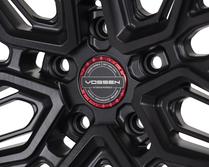 Black alloy wheel with intricate geometric design, featuring a red center cap labeled "VOSSEN HYBRID-FORGED," surrounded by text: "VOSSEN WHEELS EST. 2006 U.S.A. PASSION - PERFORMANCE - PRECISION."