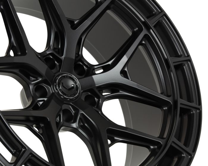 A black alloy wheel, featuring a multi-spoke design, is showcased in a close-up image. The background is plain white, highlighting the wheel's intricate patterns and sleek finish.