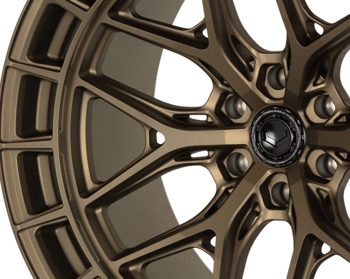 A bronze alloy wheel with intricate spoke design and a central emblem featuring the text: "VOSSEN FORGED VOSSEN WHEELS MIAMI FLORIDA." Set against a plain background.