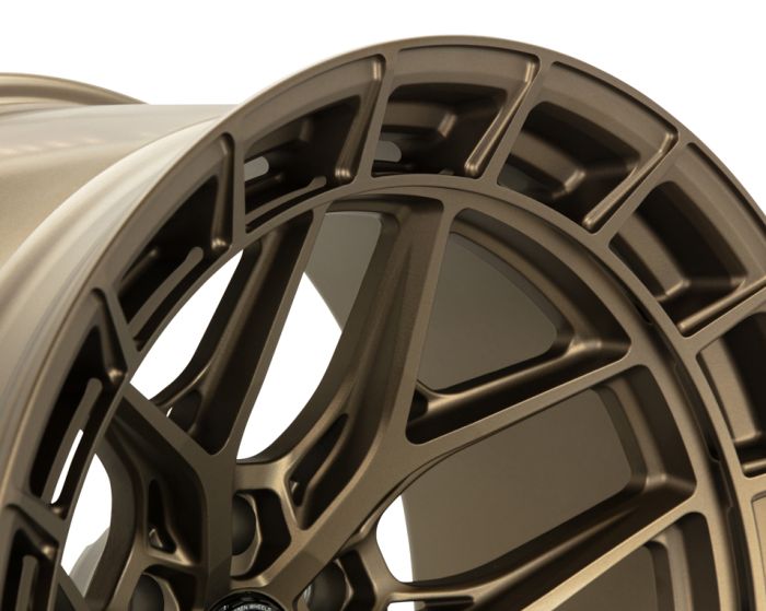 A metallic, bronze-colored car wheel rim with intricate spoke design sits against a plain background, showcasing its detailed craftsmanship and shiny finish.