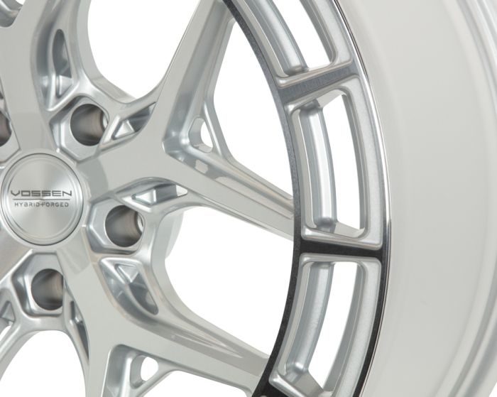 A silver alloy wheel rim, featuring intricate spoke design, engraved with "VOSSEN HYBRID FORGED," displayed against a plain white background.