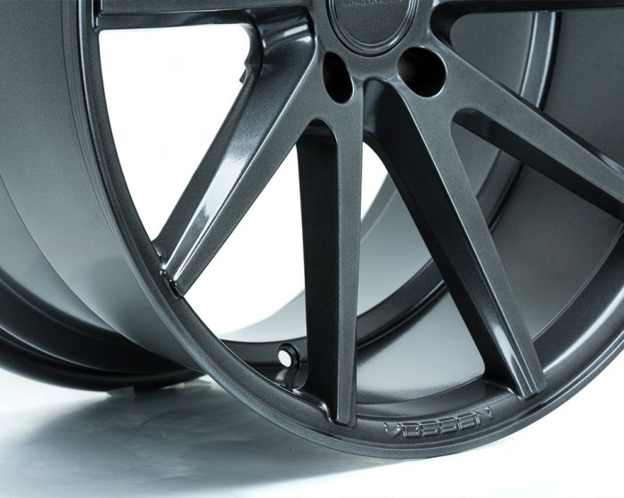 A metallic alloy wheel with angular spokes sits upright against a clean, white background. The brand name "VOSSEN" is inscribed near the rim's base.